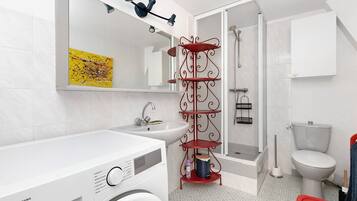Een moderne badkamer met een wit wastafelmeubel, een rode metalen plank, een toilet en een douche.
