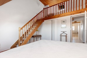 Een slaapkamer met een houten trap, een bed, een nachtkastje en een kledingkast.