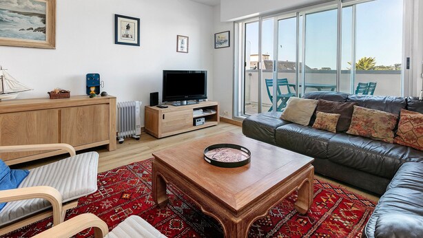 Ein Wohnzimmer mit Sofa, Couchtisch, Fernseher und Blick ins Freie.