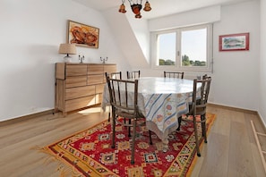 Een eetruimte met een ronde tafel, stoelen, een houten kast en een groot raam.