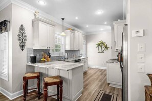 A modern kitchen with white cabinetry, a marble island, wooden stools, and a stainless steel refrigerator. - Short Walk to Beach, Waterpark and Golf Cart (Myrtle Beach)