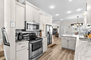 A modern kitchen with white cabinetry, stainless steel appliances, and a marble countertop. - Short Walk to Beach, Waterpark & Golf Cart (Myrtle Beach)