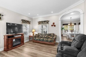 A living room with a TV, sofa, armchair, and dining area with a chandelier. - Short Walk to Beach, Waterpark & Golf Cart (Myrtle Beach)