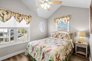 A bedroom with a bed, a ceiling fan, a window with blinds, a bedside table with a lamp, and a view of the outside. - Short Walk to Beach, Waterpark & Golf Cart (Myrtle Beach)