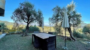 Een terras buiten met een tafel en stoelen, omgeven door bomen en een hek.