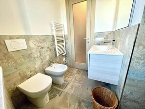 Een badkamer met toilet, bidet en wastafel met spiegel.