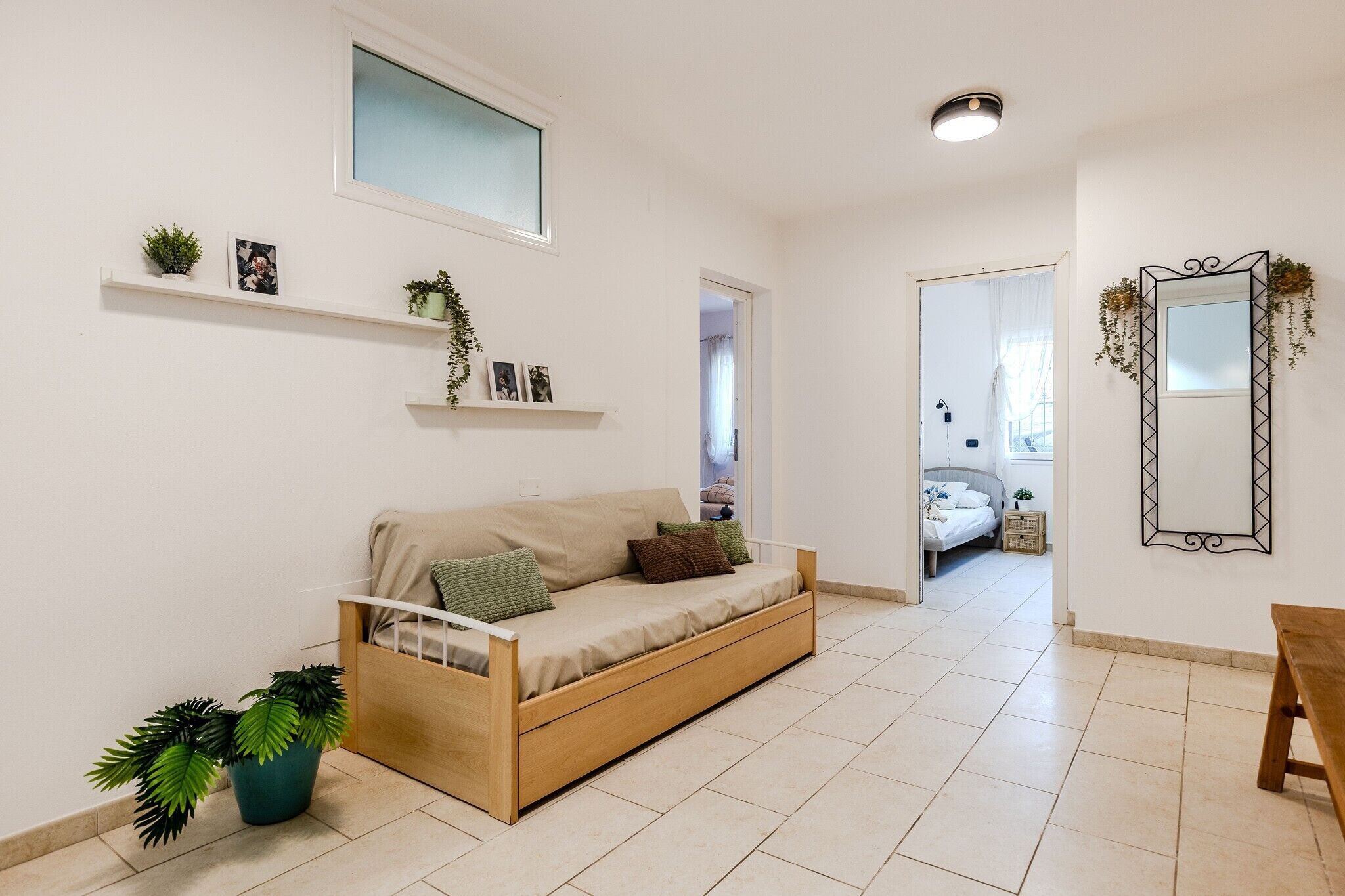 A modern living room with a sofa, a wooden bench, and a bed in the background.