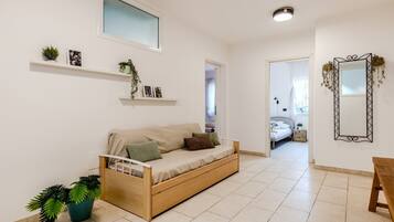 A modern living room with a sofa, a wooden bench, and a bed in the background.
