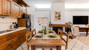 Une cuisine avec des meubles en bois, une table à manger dressée avec de l’assiette, et un téléviseur à écran plat fixé au mur.