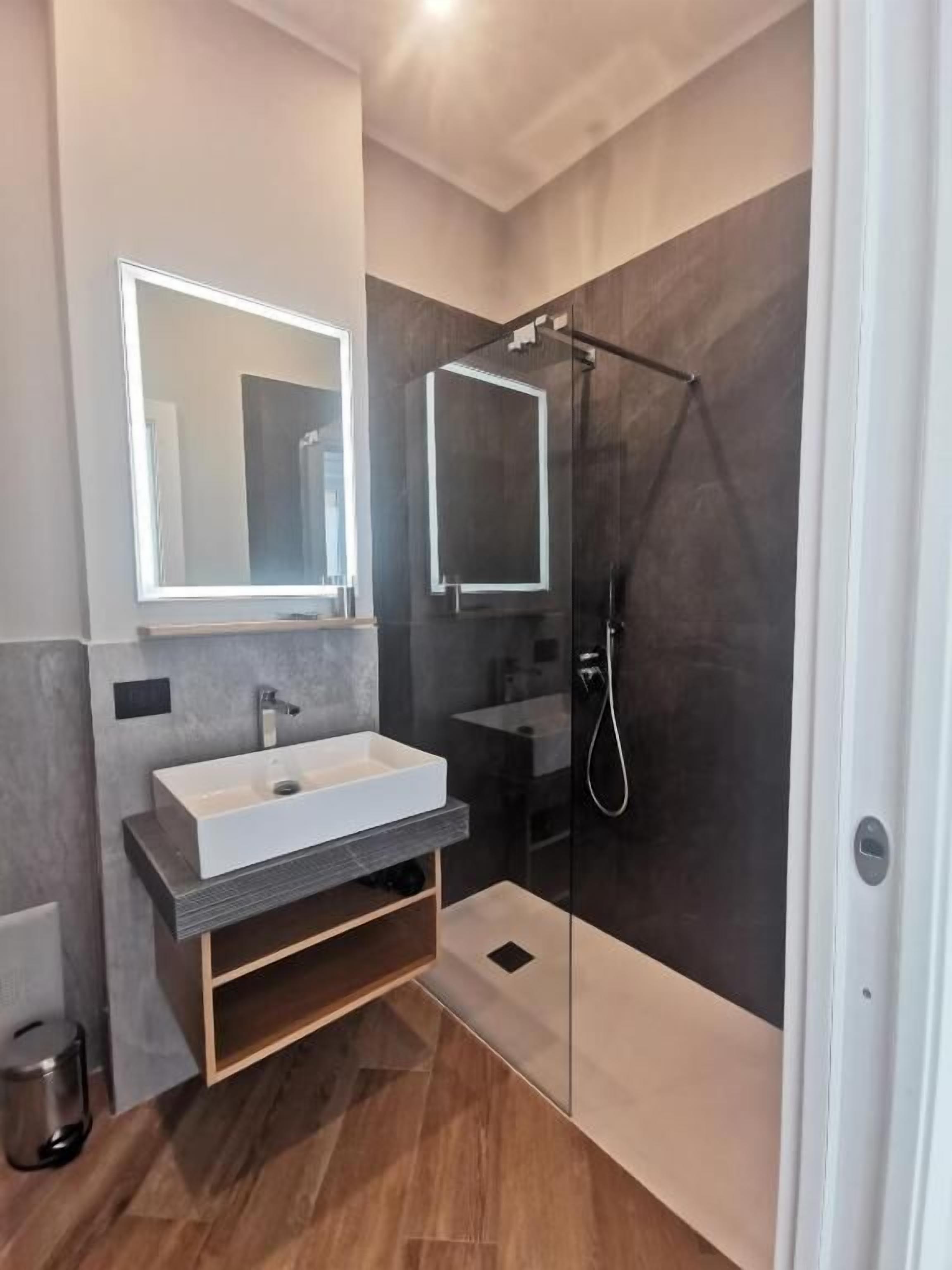 Un baño moderno con un espejo grande, un lavabo blanco y una ducha con mampara de vidrio.