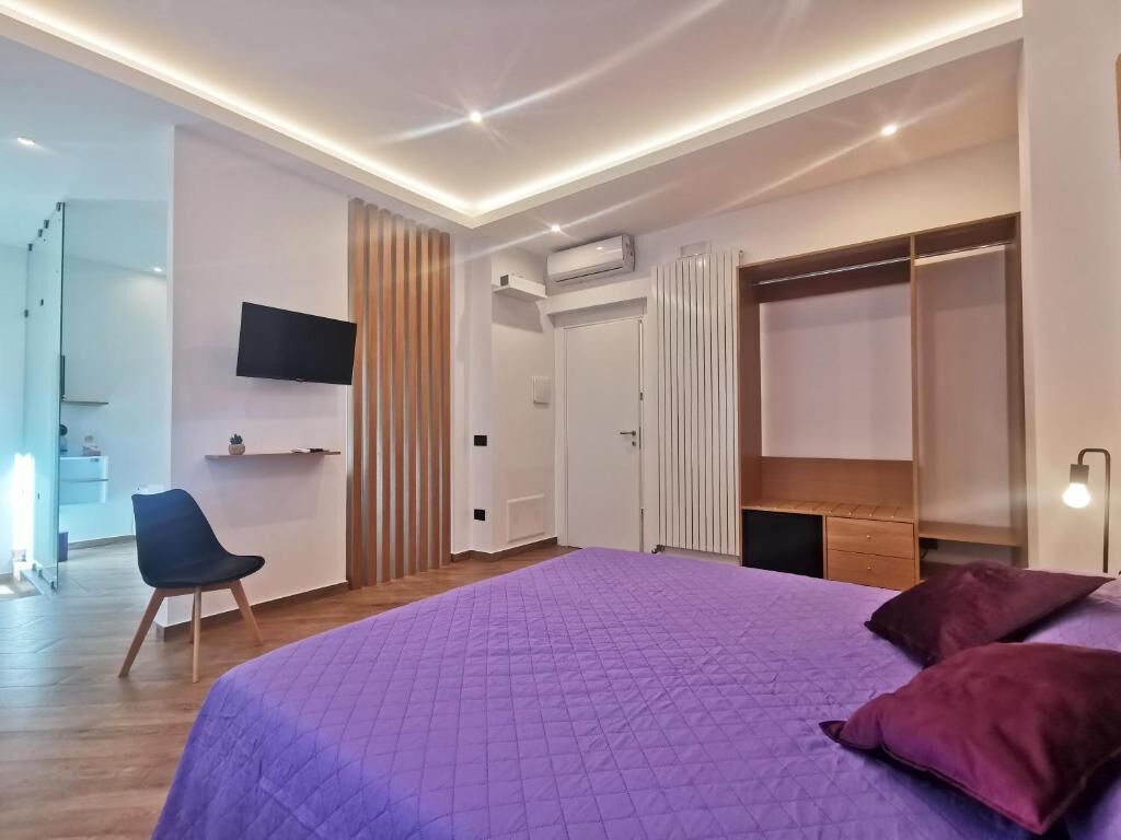 Ein modernes Schlafzimmer mit einem großen Bett, einem an der Wand montierten Fernseher, einem Kleiderschrank und einem Schreibtisch mit Stuhl.
