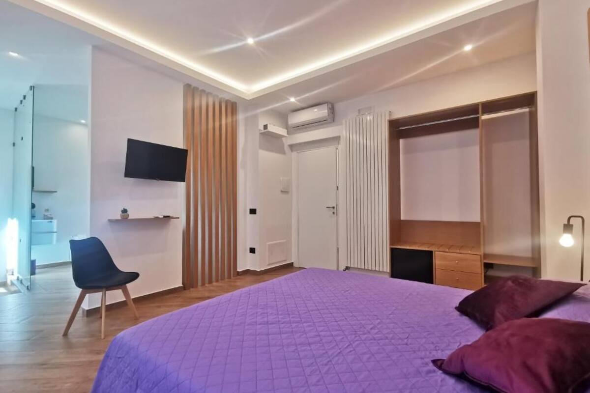 Une chambre à coucher moderne avec un grand lit, un téléviseur fixé au mur, une armoire et un bureau avec une chaise.