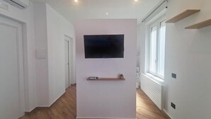 Käytävä, jossa on seinälle asennettu taulutelevisio, puulattia ja valkoiset seinät.