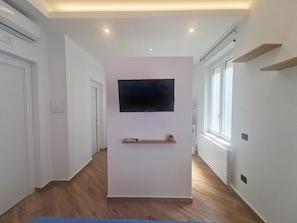 Ein Korridor mit einem an der Wand befestigten Flachbildfernseher, Holzdielen und weißen Wänden.