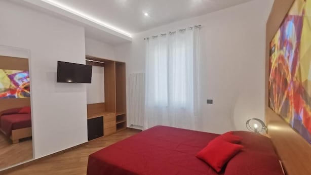 Moderni hotellihuone, jossa on suuri sänky, televisio, puinen vaatekaappi ja ikkuna, jossa on verhot.