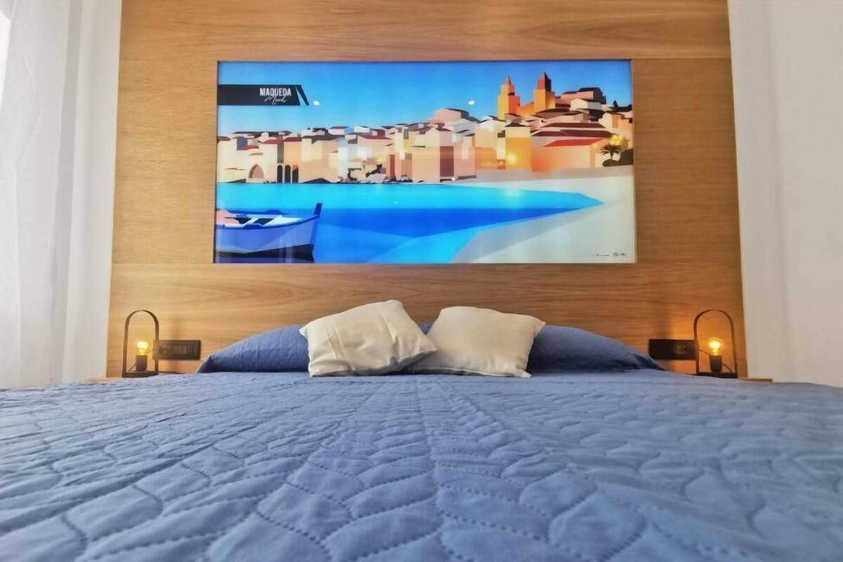 Un lit recouvert d’une couverture matelassée bleue, avec deux oreillers, et un téléviseur fixé au mur qui diffuse une vue sur la ville.