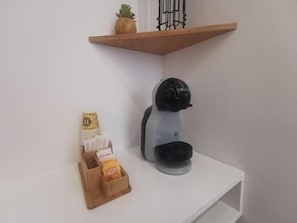 Ein weißes Regal mit einer Kaffeemaschine, einer Holzkiste mit Snacks und einer Ananas auf einem Holzregal darüber.