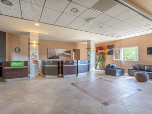 A hotel lobby with a reception desk, seating area, and a large window with a view of greenery.