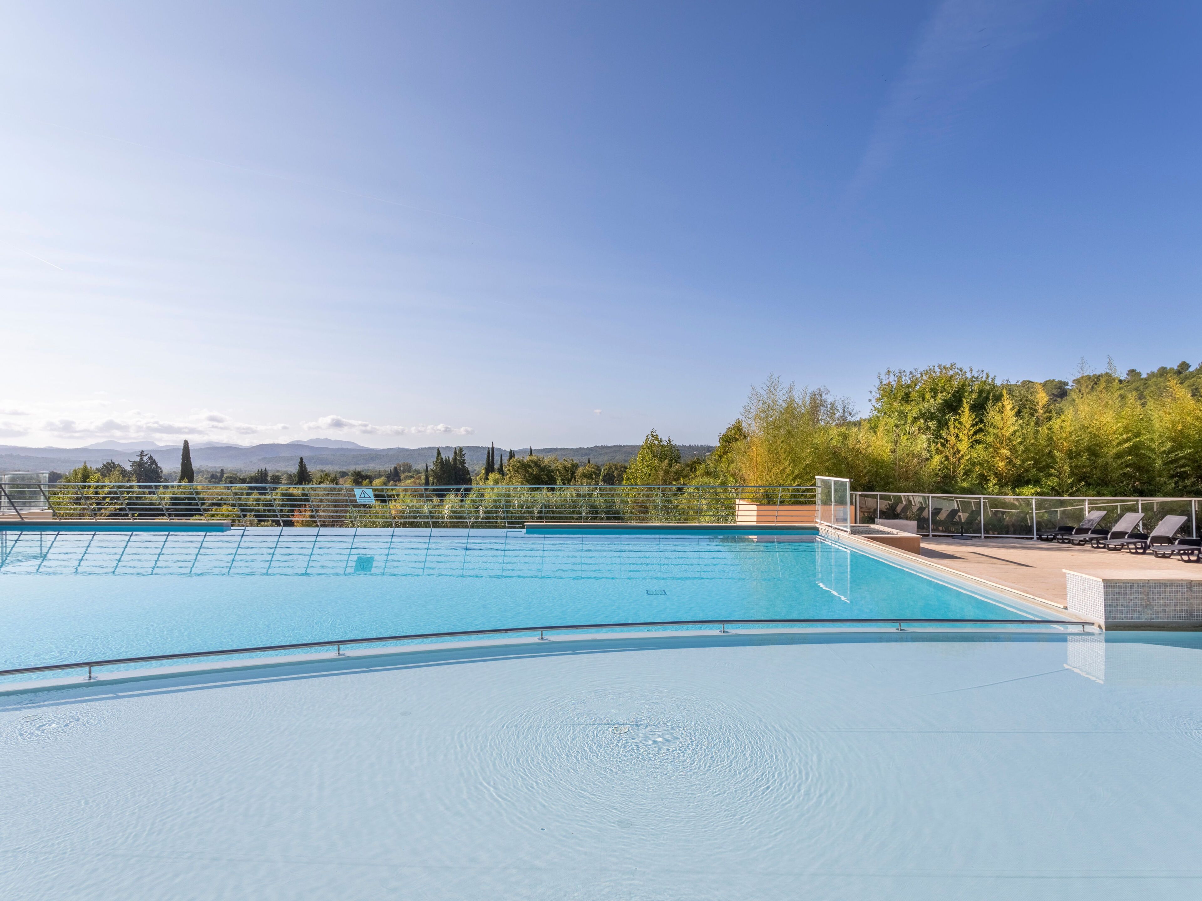 Une piscine d’eau cristalline, d’un bleu éclatant, avec en arrière-plan une vue sur des montagnes et des arbres.