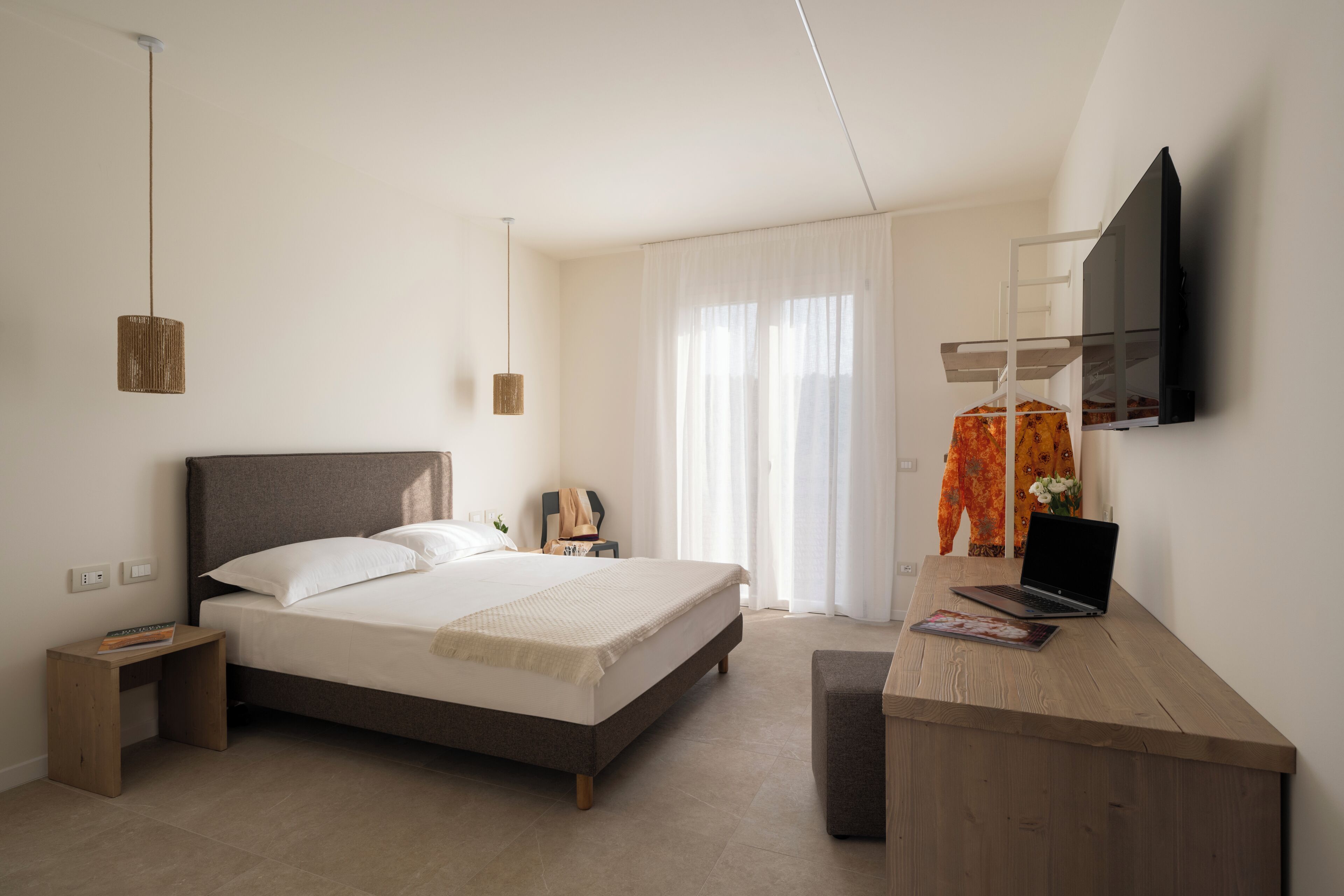A bedroom with a bed, bedside table, lamp, TV, and a desk with a laptop.