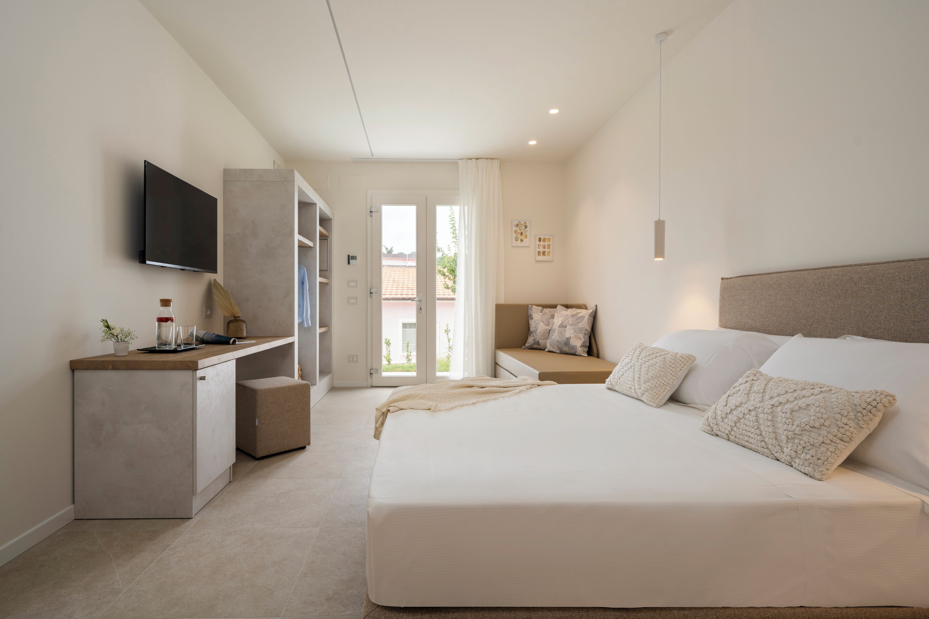 A bedroom with a bed, a TV, a desk, and a view of the outside.