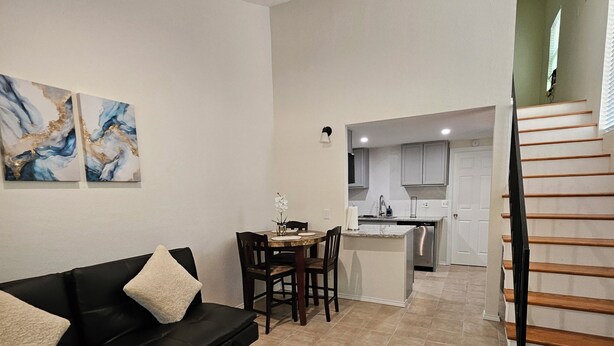 A living room with a black sofa, a dining table, and a kitchen in the background. - 4min to World Cup Stadium/Dallas Stadium - 0.9 mile from AT&T Stadium Arlington (Arlington)