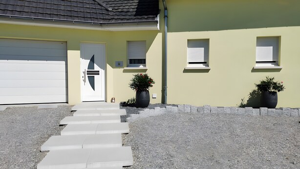 Ein Wohngebäude mit Garage, einer Haustür, zwei Fenstern und einer Treppe zum Eingang.