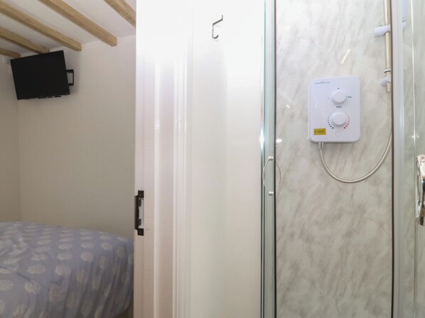 A bathroom with a glass shower enclosure, a control panel, and a bed with patterned bedding. - 61A High Street (Criccieth)