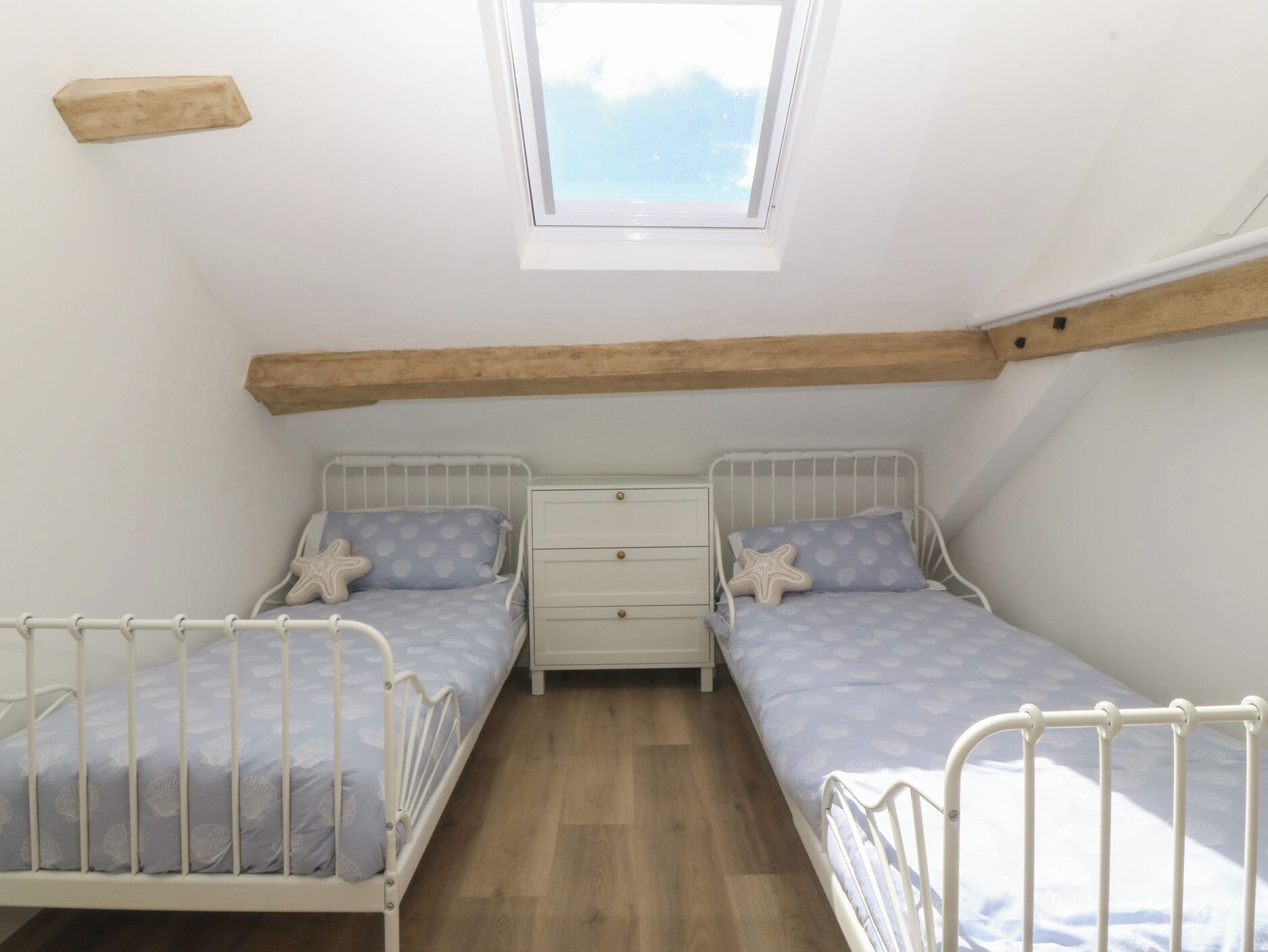 Eine kleine, einfache Unterkunft mit zwei Betten, einem Nachttisch, einem Fenster und Holzbalken an der Decke.
