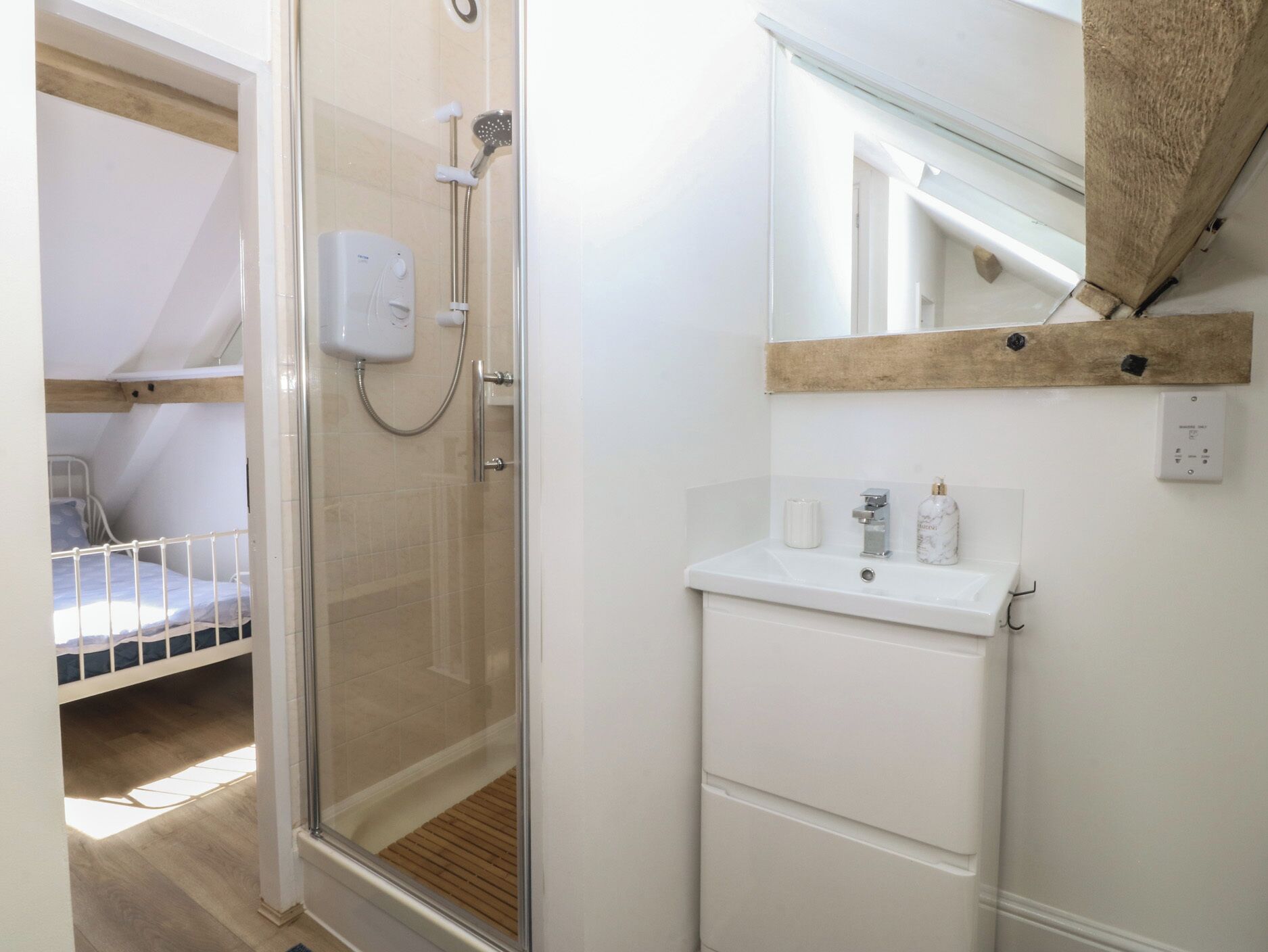 Una habitación pequeña con ducha, lavamanos y cama.