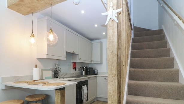 A kitchen with white cabinets, a wooden island with stools, a staircase, and a wooden ceiling.