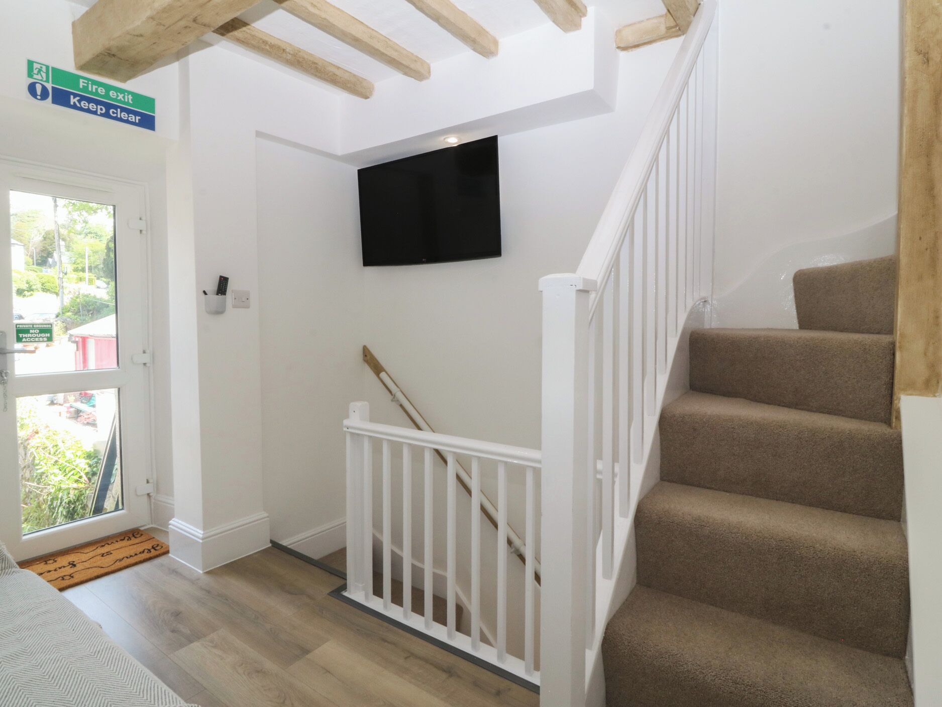 A staircase with a white railing, a fire exit sign, and a television mounted on the wall.