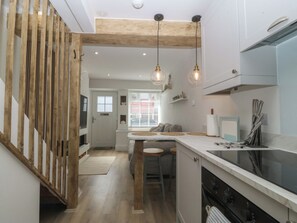 A modern kitchen with wooden beams, pendant lights, a central island, and a built-in oven. - 61A High Street (Criccieth)