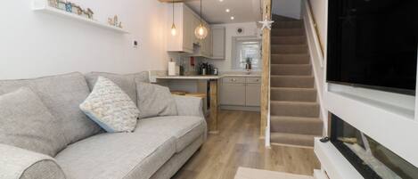 A modern living space with a sofa, a kitchen area, and a staircase leading to a darkened room.
