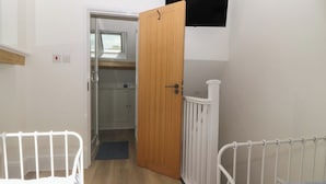 A bedroom with a wooden door, a white railing, and a TV mounted on the wall.