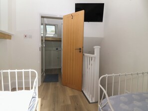 A bedroom with a wooden door, a white railing, and a TV mounted on the wall.