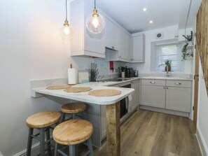 A modern kitchen with a central island, bar stools, and pendant lighting. - 61A High Street (Criccieth)