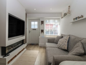 A living room with a flat-screen TV, a grey sofa, a white door, and a window with blinds.
