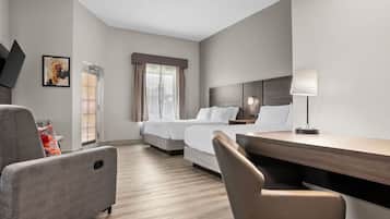 Quarto de hotel com cama, escrivaninha, cadeira, luminária e um quadro na parede.