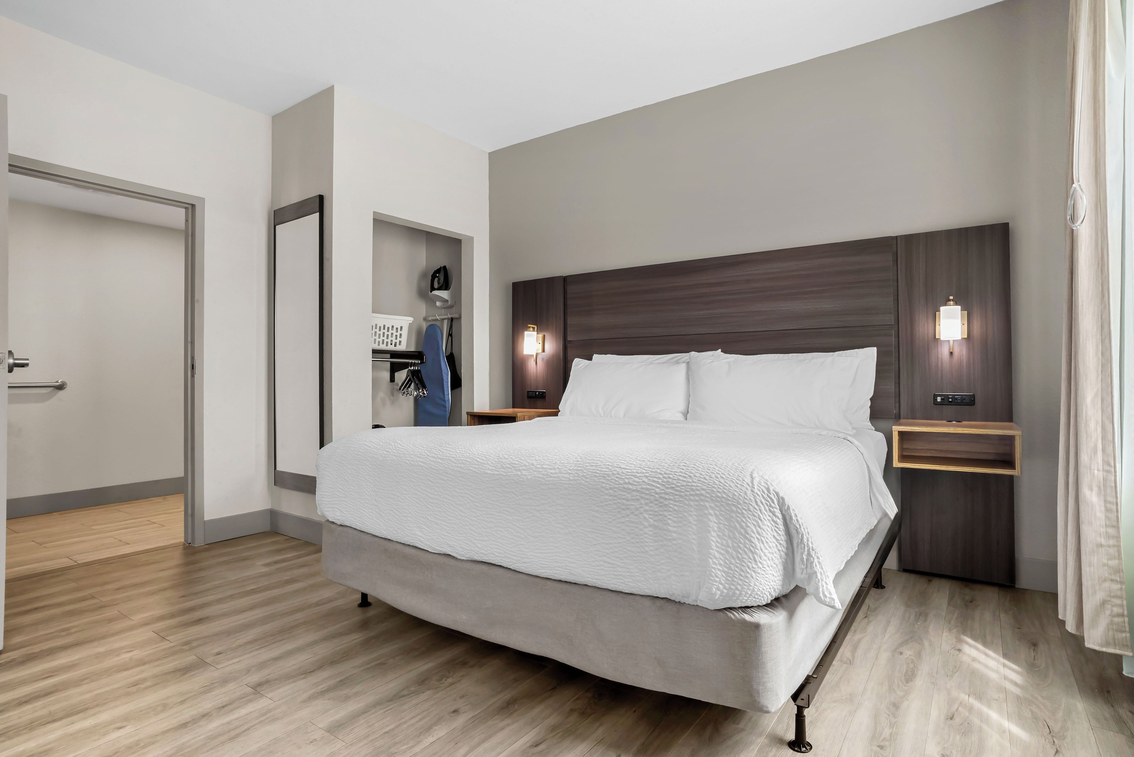 A modern hotel room with a large bed, wooden flooring, a wardrobe, and two bedside tables with lamps.