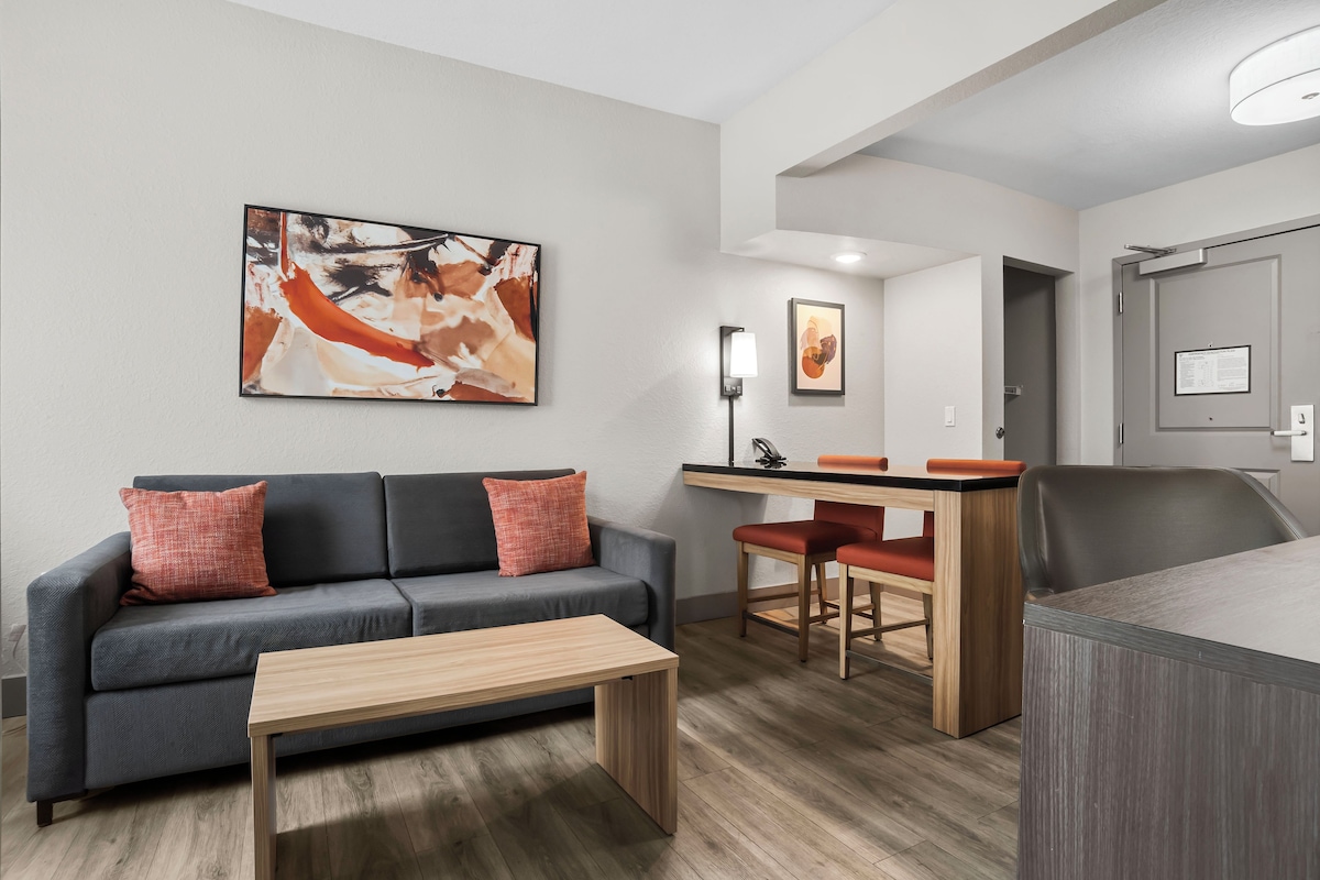 A modern living room with a grey sofa, a wooden coffee table, and a painting on the wall.