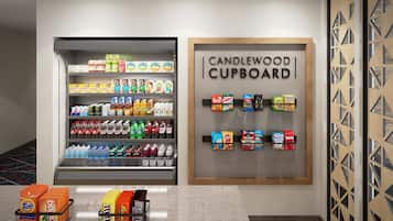 A beverage display with various drinks and snacks, a sign reading 'CANDLEWOOD CUPBOARD,' and a section with Tide and Bounce laundry detergent.