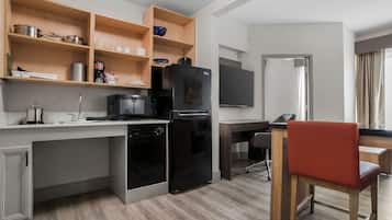 Cocina compacta con refrigerador, microondas y lavavajillas. Hay una mesa de madera con una silla, y un televisor de pantalla plana montado en la pared.
