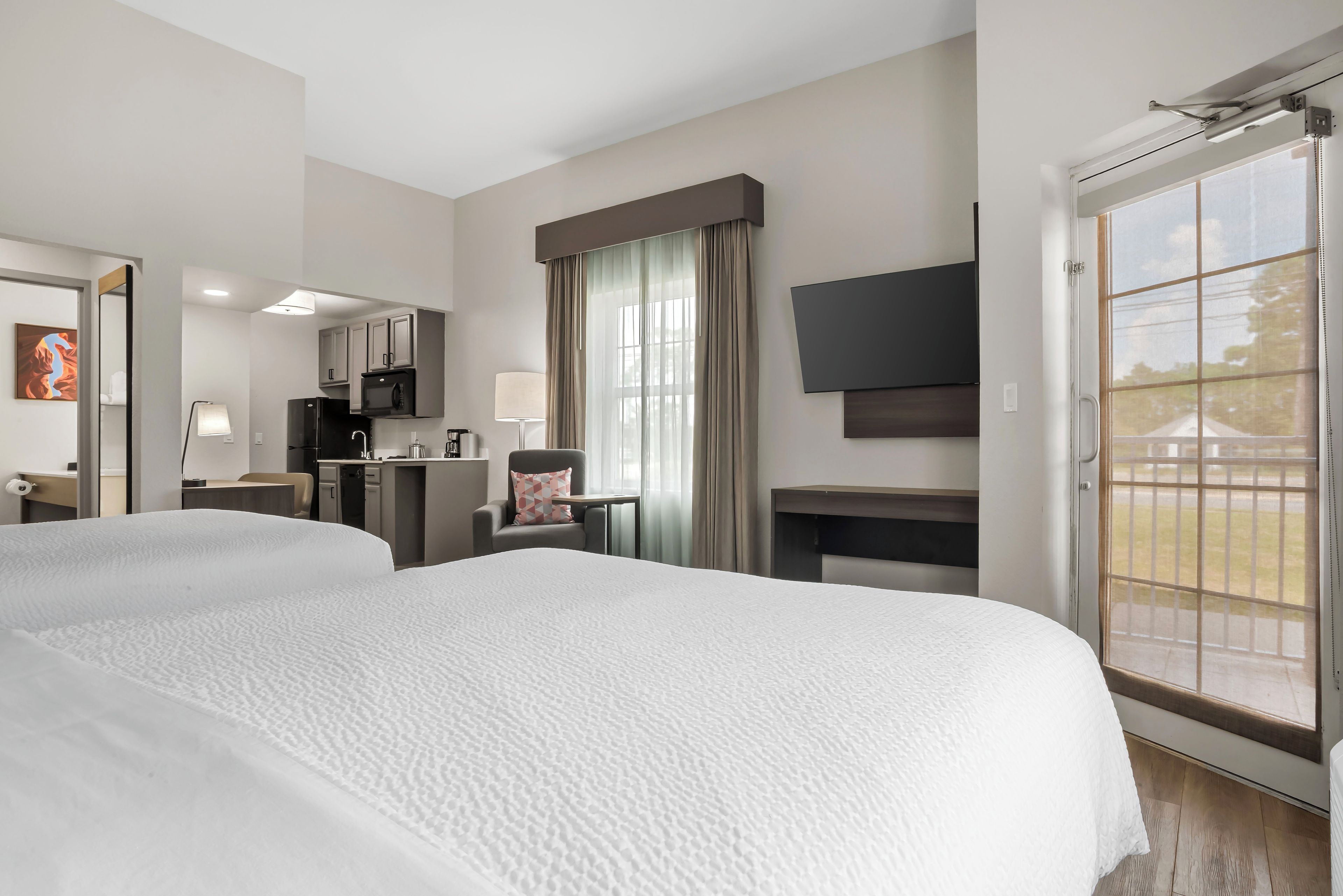 A hotel room with two beds, a kitchenette, a TV, and a large window.