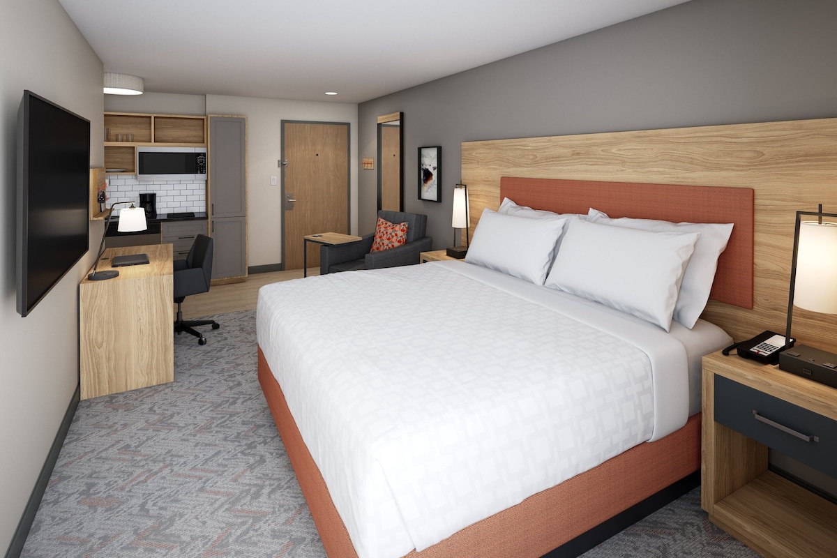 Quarto de hotel com cama, escrivaninha, cadeira, televisão, micro-ondas e porta para o banheiro.