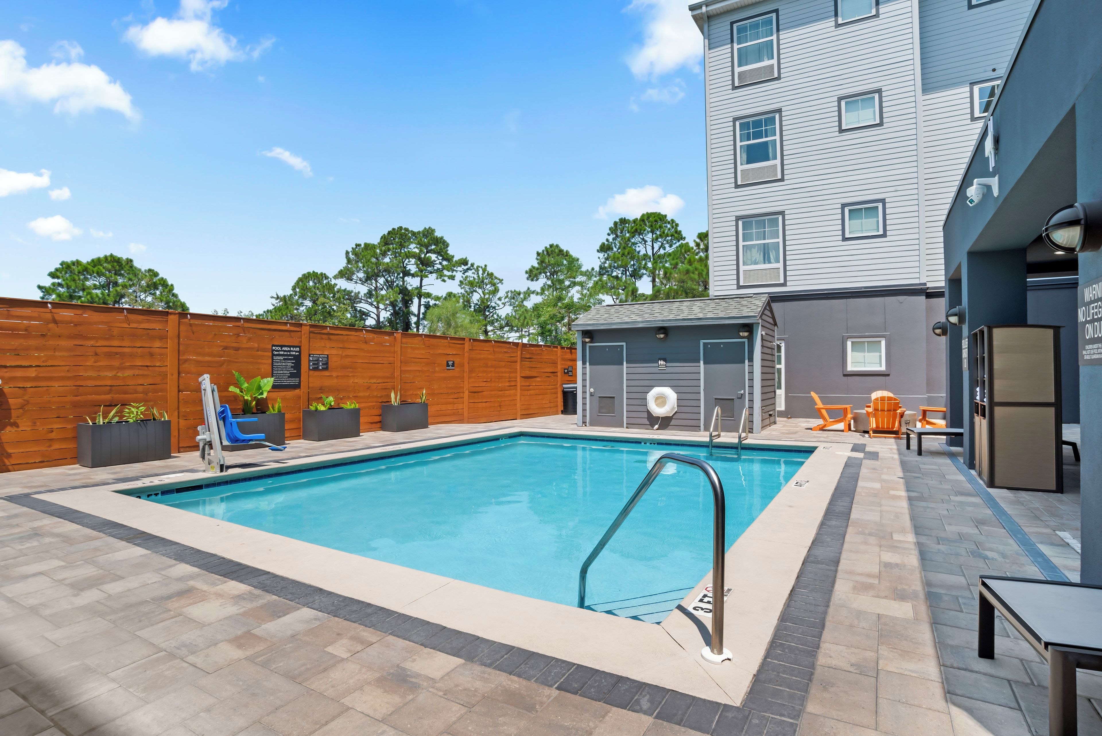 A rectangular swimming pool with a metal ladder, surrounded by a wooden fence and potted plants.