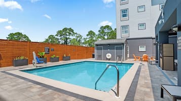 A rectangular swimming pool with a metal ladder, surrounded by a wooden fence and potted plants.