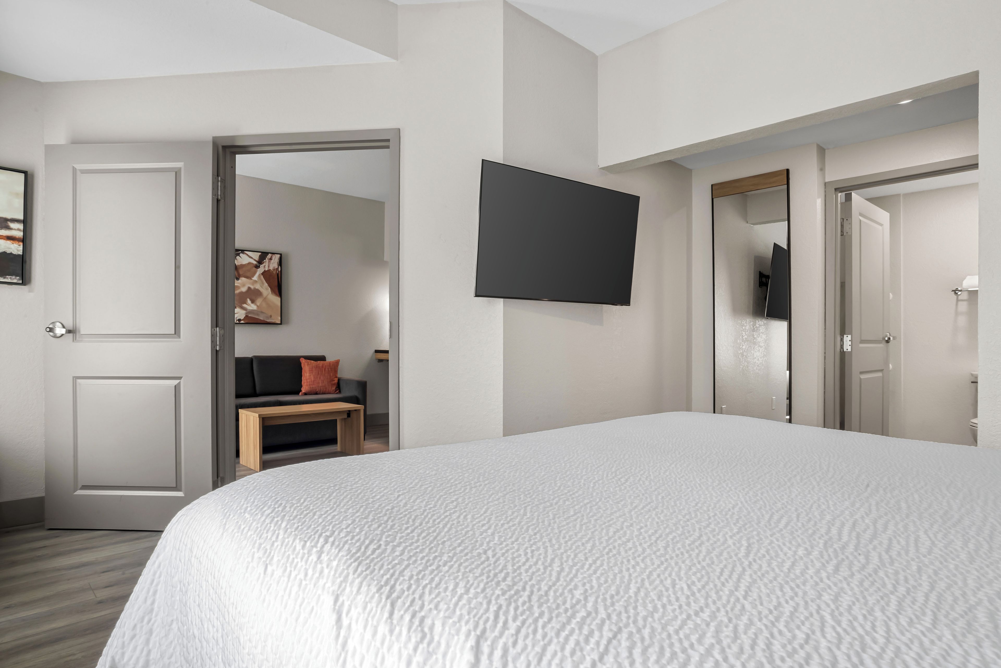 A hotel room with a large bed, a flat-screen TV mounted on the wall, a sofa with cushions, and a door leading to a bathroom.