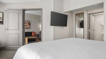A hotel room with a large bed, a flat-screen TV mounted on the wall, a sofa with cushions, and a door leading to a bathroom.
