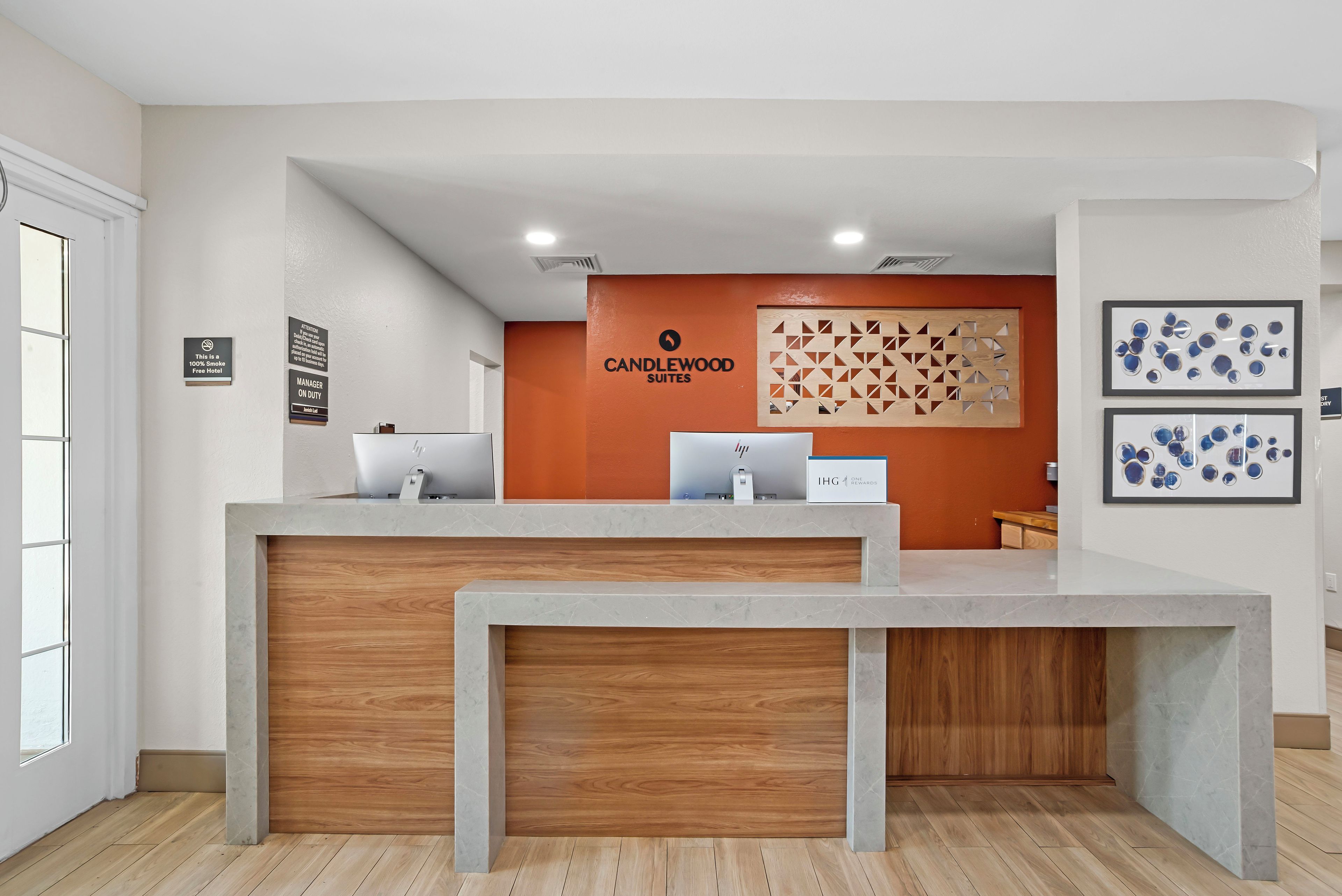 Un mostrador de recepción con panel de madera, un letrero de Candlewood Suites y una pared con diseños geométricos.